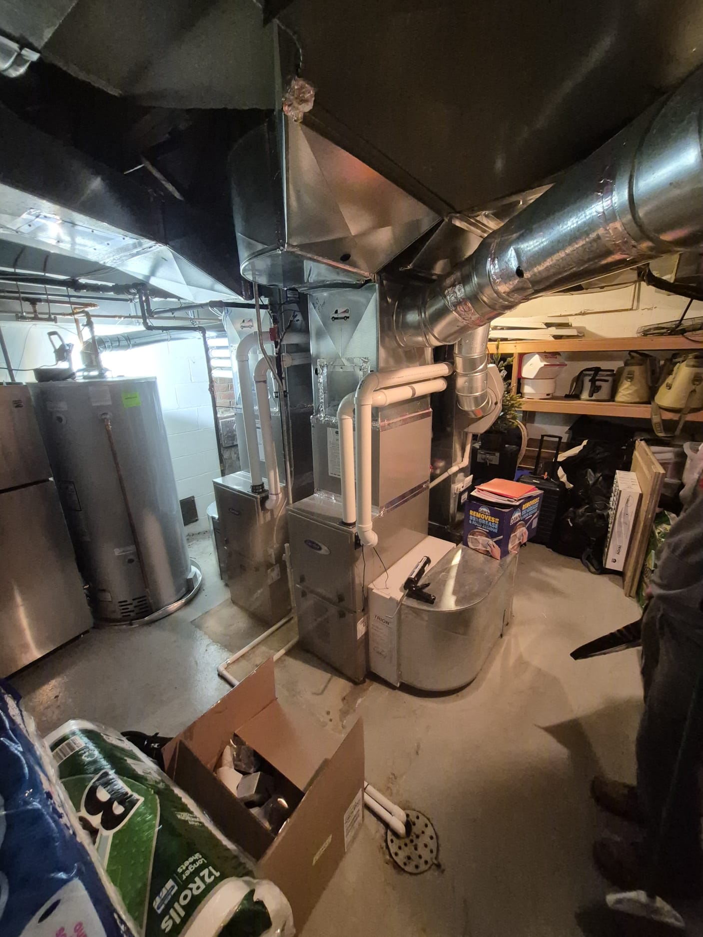 Basement with water heaters, HVAC system, ductwork, and storage shelves. Cardboard boxes and miscellaneous items are scattered on the floor. | C & C Heating & Air Conditioning