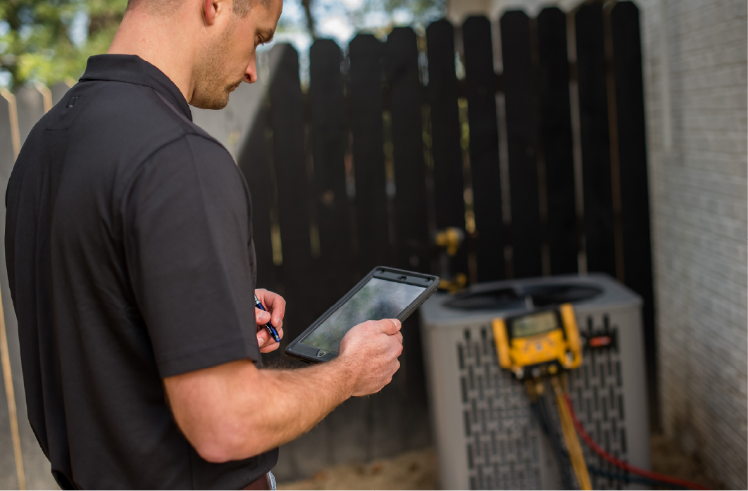 A technician in a black shirt uses a tablet while inspecting an outdoor HVAC unit with attached diagnostic equipment to help improve indoor air quality. | C & C Heating & Air Conditioning