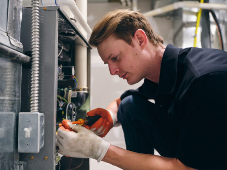 A technician wearing gloves uses a screwdriver to repair or inspect electrical components inside an industrial heating system. | C & C Heating & Air Conditioning